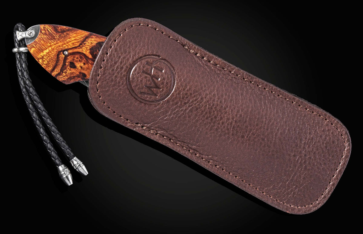 Luxury B12 Wrangler knife with rich wood grain handle, partially sheathed in dark brown leather with embossed logo and braided cord lanyard, side view.