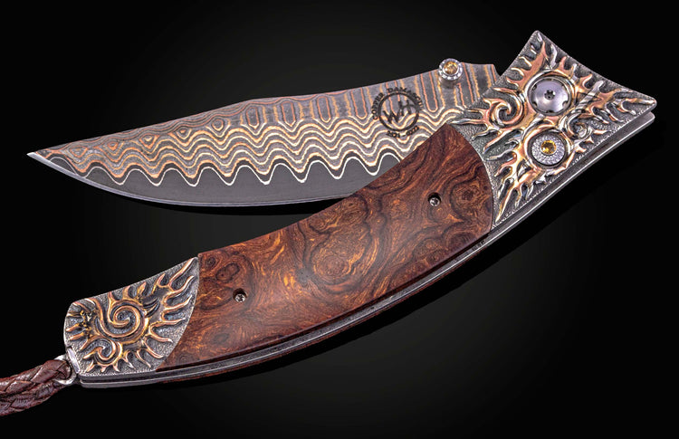 Ornate folding knife with wavy copper Damascus blade, dark burled wood handle, and silver sunburst bolsters with gems and a leather lanyard.
