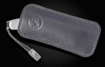 Silver-toned knife handle in a dark, textured leather case with an embossed design and a braided strap featuring a metallic skull charm.