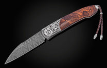 Damascus steel knife with intricate silver flame inlays and rich wood handle, featuring braided leather lanyard, side view on black background