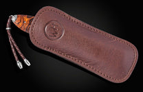 Brown leather sheath with embossed logo and braided cord, featuring a wooden knife handle with silver accents, side view.