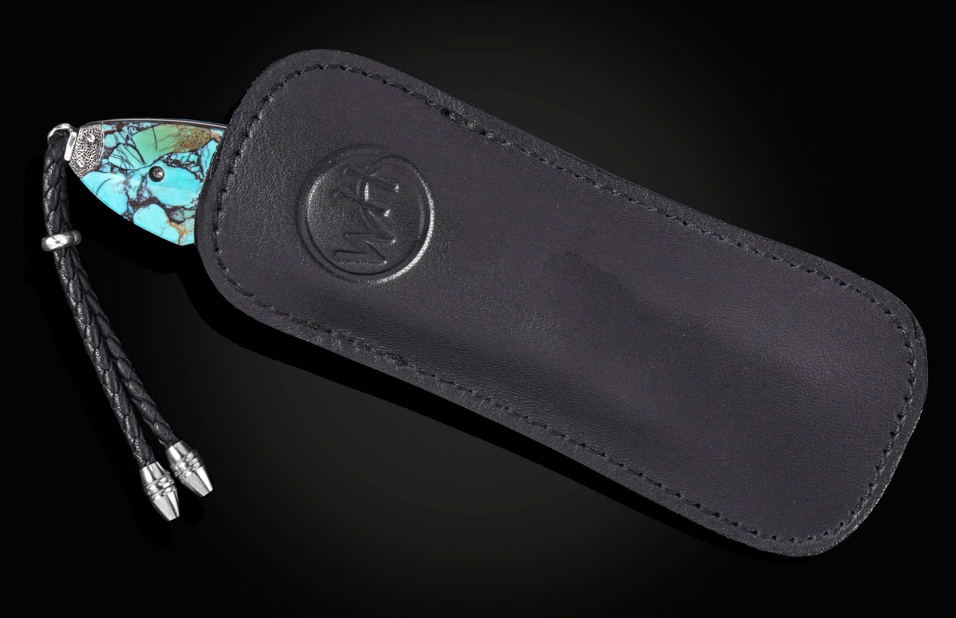 Knife with a turquoise stone handle, silver accents, and a black braided leather lanyard, partially in a black leather sheath with an embossed logo.