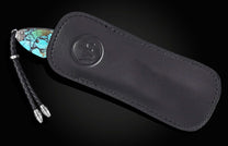 Knife with a turquoise stone handle, silver accents, and a black braided leather lanyard, partially in a black leather sheath with an embossed logo.
