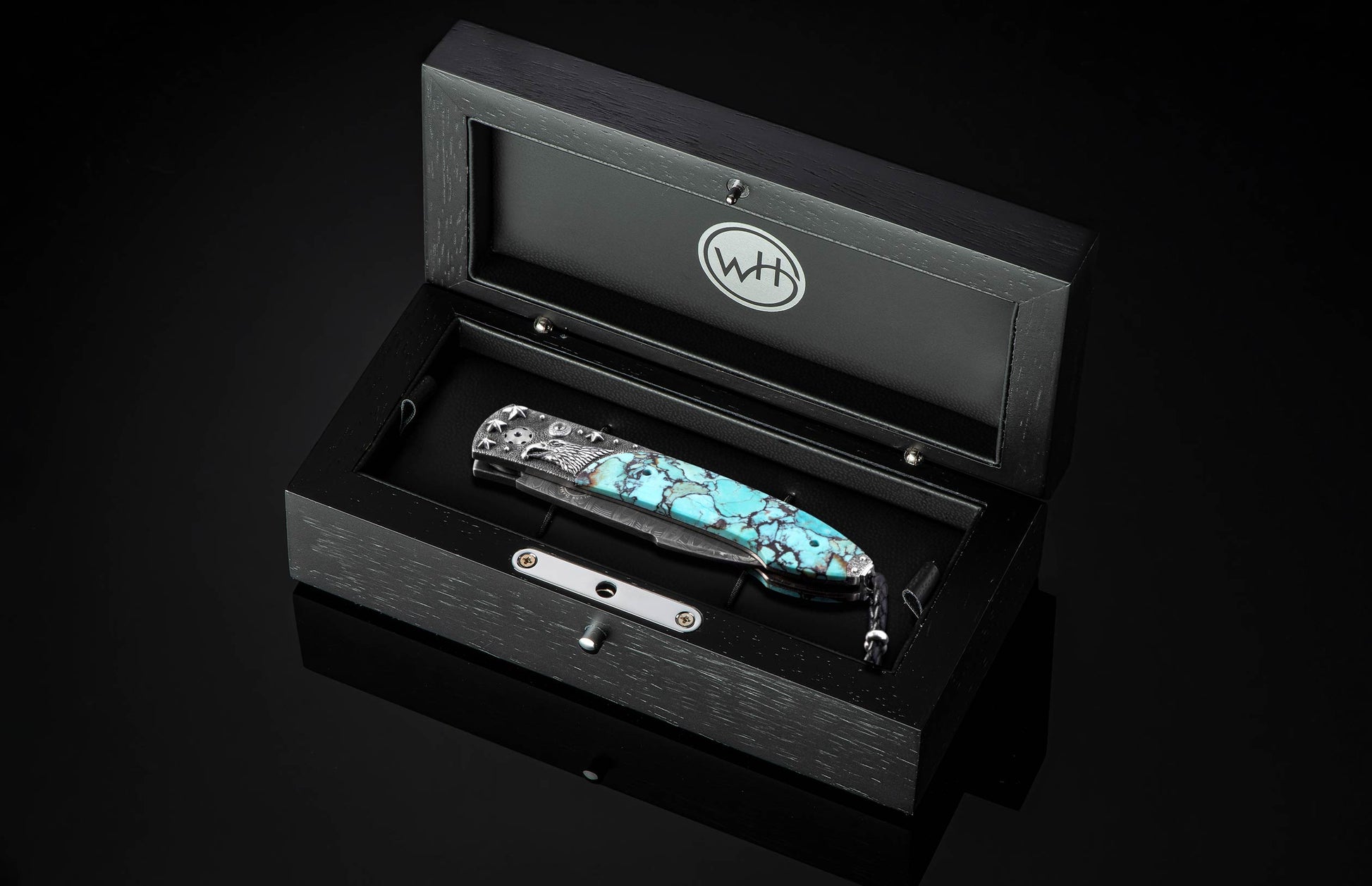 Automatic pocket knife with turquoise handle and silver eagle engraving from William Henry, with a Damascus blade, presented in an open black wooden box.