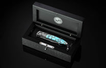 Automatic pocket knife with turquoise handle and silver eagle engraving from William Henry, with a Damascus blade, presented in an open black wooden box.