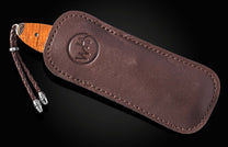 Brown leather sheath with embossed logo, by B22 Sunset, featuring wooden knife handle and braided cord with metal tips, side view.