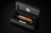 Luxury B22 Sunset folding knife with rich amber wood handle, by W.H. in elegant black presentation box, top-down view
