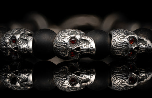 Sterling silver skull bracelet with garnet eyes and matte black beads, featuring a detailed reflective surface.