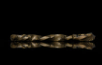 Twisted mokume-gane ring with golden and dark layered patterns, side view on reflective black surface