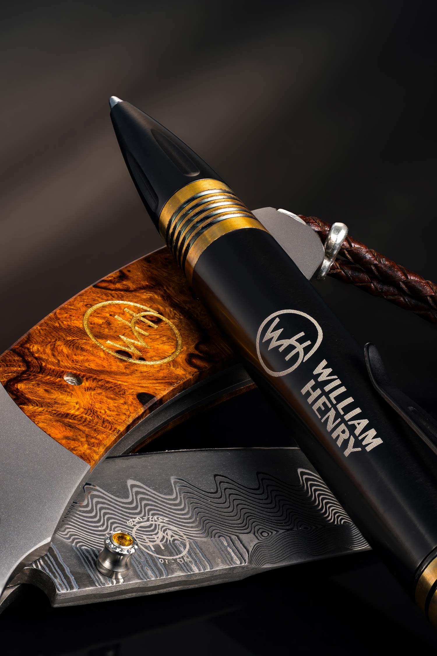 Pen with gold accents and 'William Henry' branding  and pocket knife on a dark background