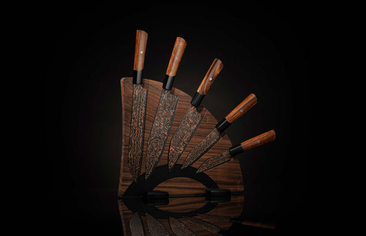 K22-BLK-W|Set of chef knives with black blades and copper rose pattern, brown wooden handles, fanned on a dark wooden block with a reflection.
