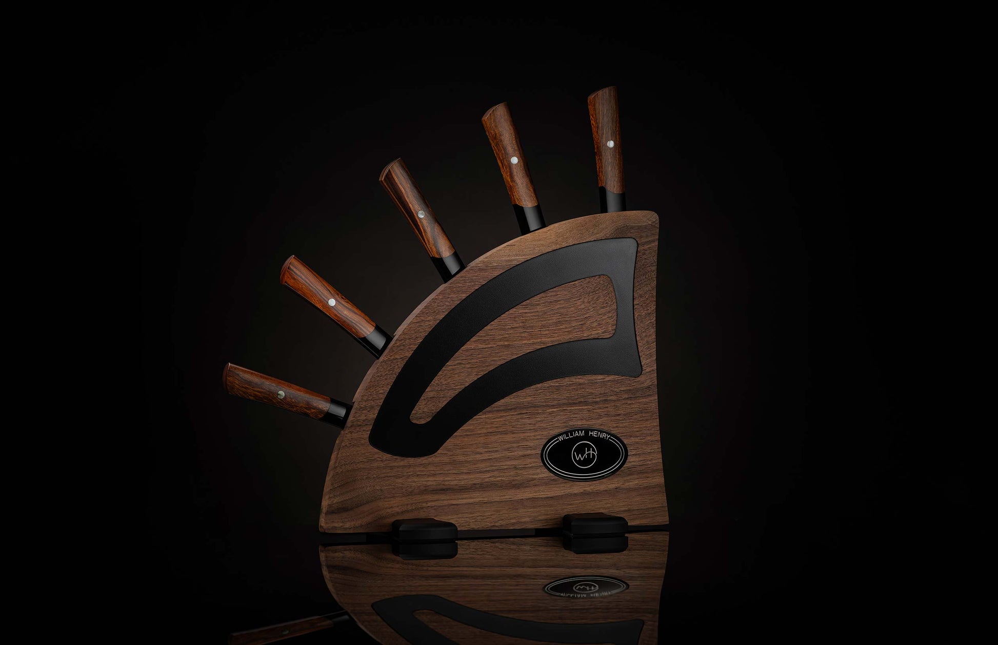 Set of black flare chef knives with wood grain handles in a 'William Henry' dark wood block with black accents.