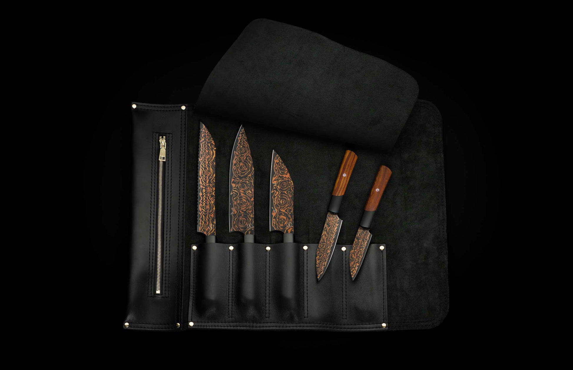 Five chef knives with black flare patterned blades, displayed in an open black leather roll-up case with gold accents.