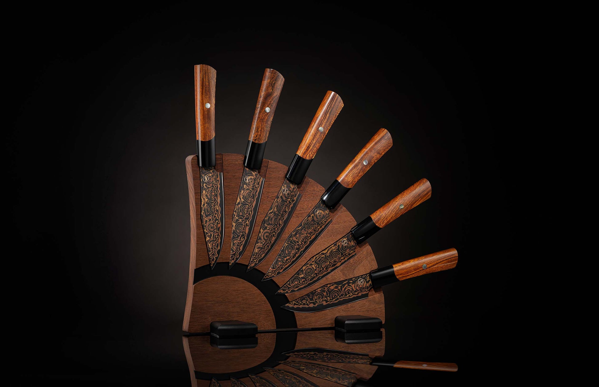  set of steak knives on a wooden blockSix steak knives with dark wooden handles, black blades with golden swirl patterns, in a fanned-out magnetic wooden block.