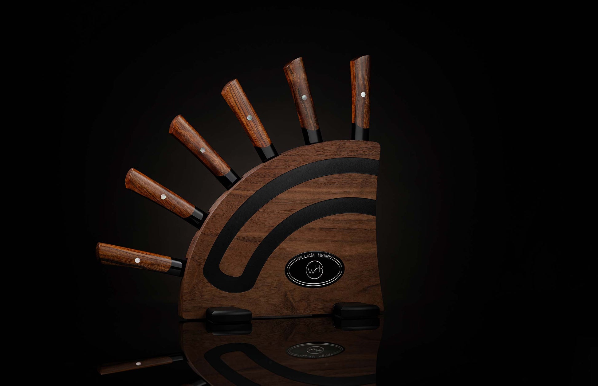  set of steak knives on a dark wooden blockSix dark wood steak knives by William Henry, with black flare handles, housed in a curved wooden block with black inlays.