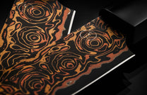 K22S-BLK-W|swirled pattern in knife bladeTwo black steak knives with textured orange and gold swirling patterns, a white logo, and polished blades.