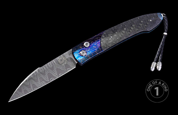 Automatic folding knife with a dark carbon fiber handle, iridescent blue patterned bolsters, a wavy Damascus blade, and a black leather lanyard with silver tips.