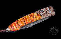 Folding knife with cracked orange and striped metallic handles, a patterned blade, and a brown braided leather lanyard.