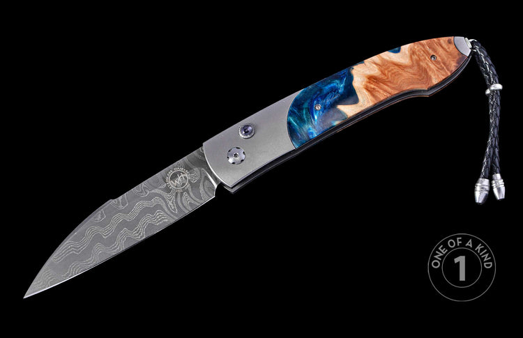 Folding knife with a wavy Damascus steel blade, blue resin and wood handle, and black braided lanyard.