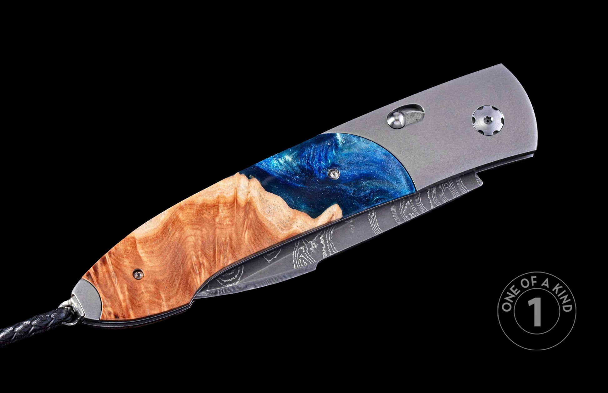 Folding knife featuring a handle of natural burl wood and sparkling blue resin, with a grey titanium frame, a Damascus steel blade, and a black braided lanyard.