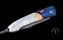 Folding knife with white mother-of-pearl and blue-purple patterned titanium handle, Damascus steel blade, and braided black leather lanyard.