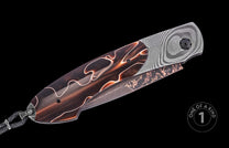 Luxury folding knife with amber-streaked resin handle and damascus steel blade, side view, one of a kind