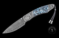 Luxury folding knife with damascus steel blade and blue resin handle, by W.H. Knives, featuring intricate silver inlays and braided lanyard, side view