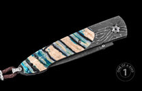 Luxury folding knife with damascus steel blade and blue-veined resin handle, featuring intricate wave patterns and a braided leather lanyard, side view.
