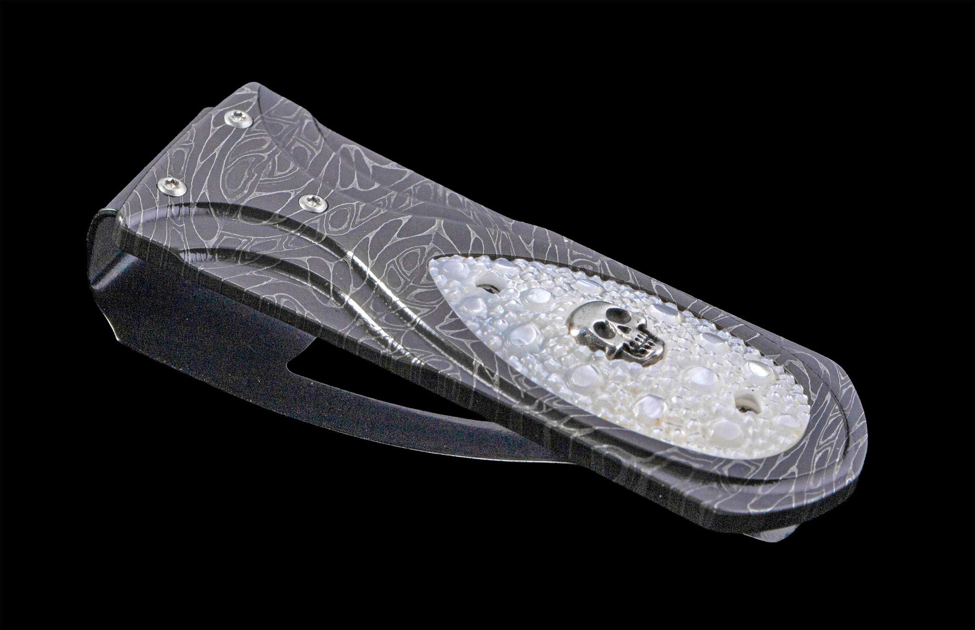 Ornate dark metal money clip with a swirling pattern, a white textured inlay, and a silver skull emblem.