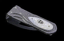Ornate dark metal money clip with a swirling pattern, a white textured inlay, and a silver skull emblem.