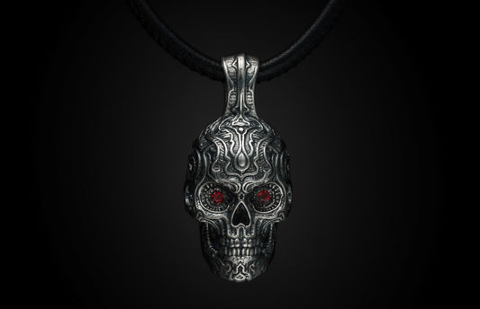 Silver skull pendant with garnet eyes and tribal engravings, suspended on a black leather cord.