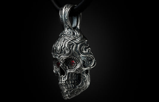Oxidized silver skull pendant with garnet eyes, featuring intricate filigree and hanging from a black leather cord.