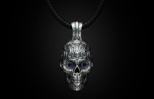 Silver skull pendant with sapphire eyes by Sapphire Renegade, featuring intricate tribal engravings on a black cord.