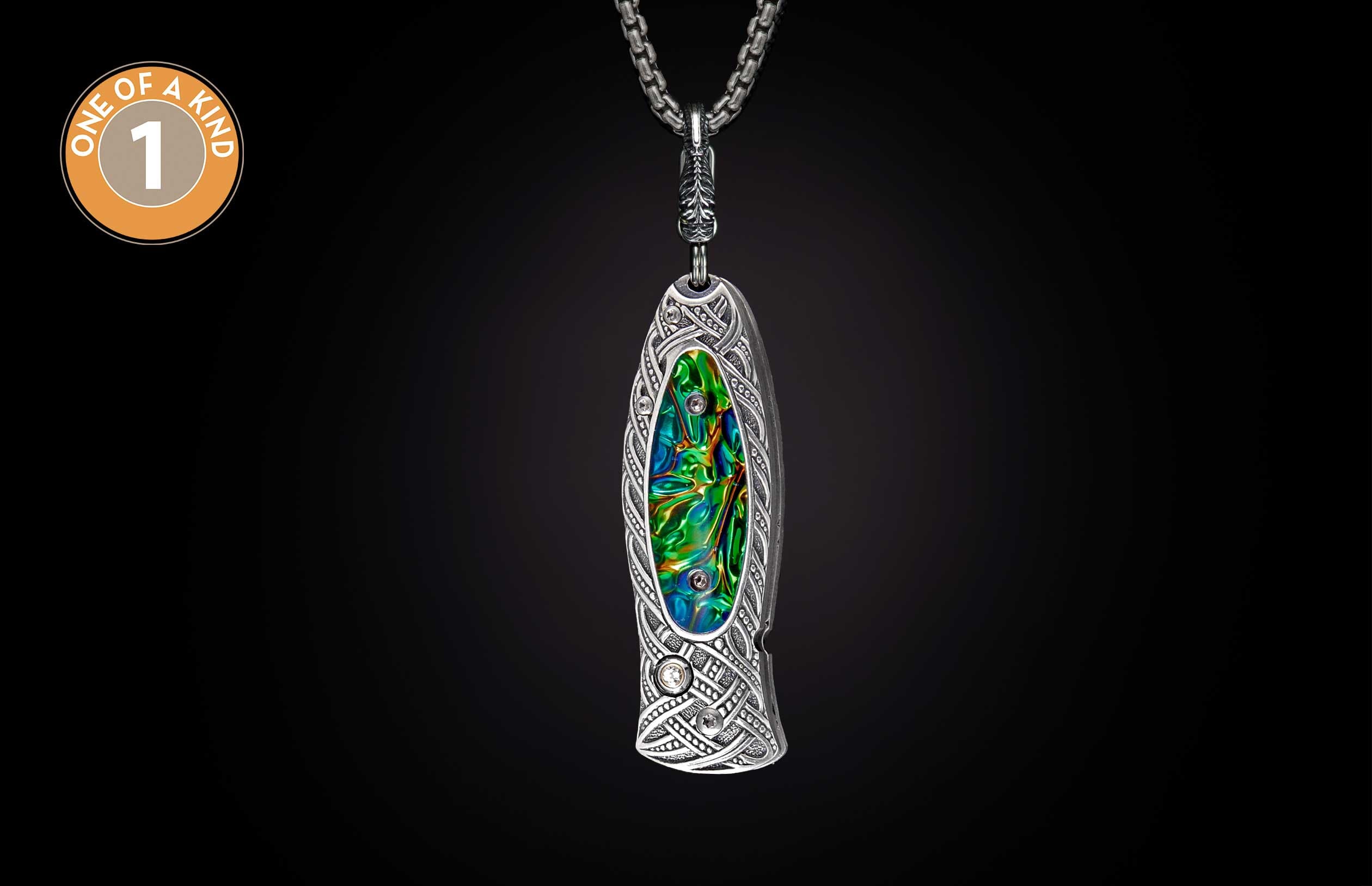 Ornate silver knife with intricate Celtic patterns and iridescent green-blue inlay, accented with clear gems, hanging from a chain.