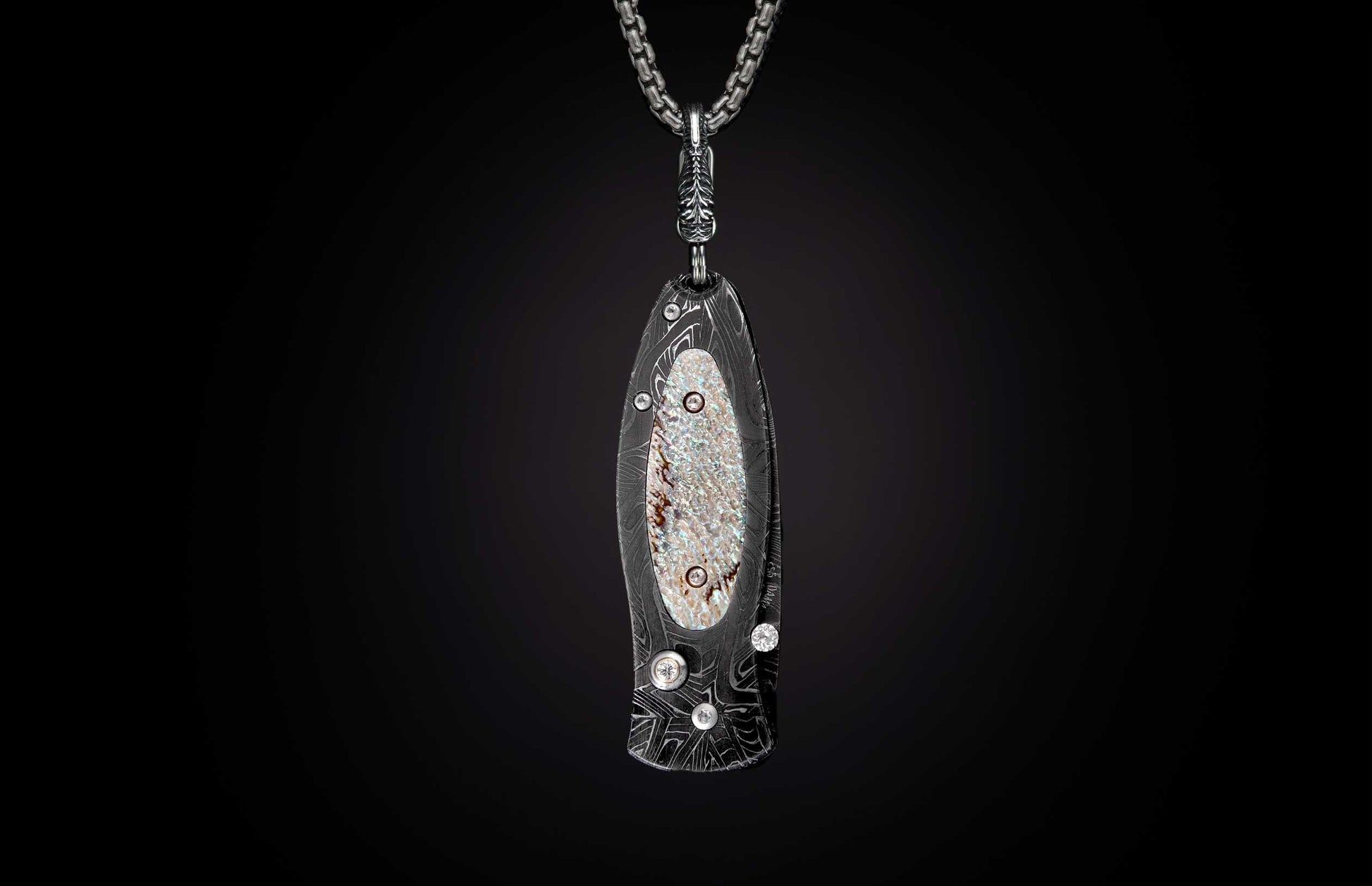 Stylized dark metal knife pendant with wavy Damascus pattern, iridescent mother-of-pearl inlay, and clear stones on a silver chain.