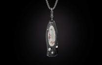Stylized dark metal knife pendant with wavy Damascus pattern, iridescent mother-of-pearl inlay, and clear stones on a silver chain.