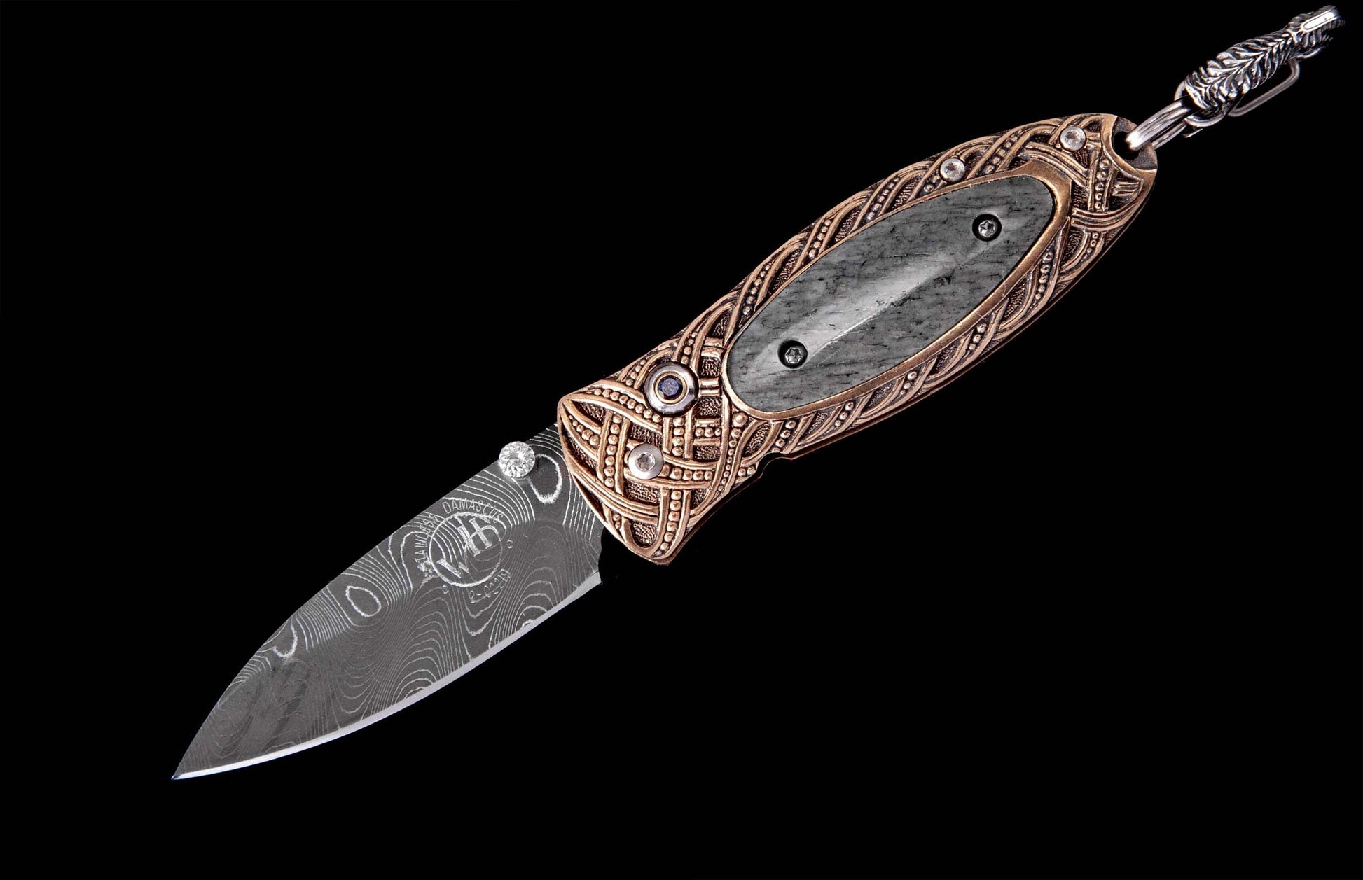 Ornate folding knife featuring a Celtic-inspired bronze handle with gray stone inlay, Damascus steel blade, and leaf-carved lanyard.