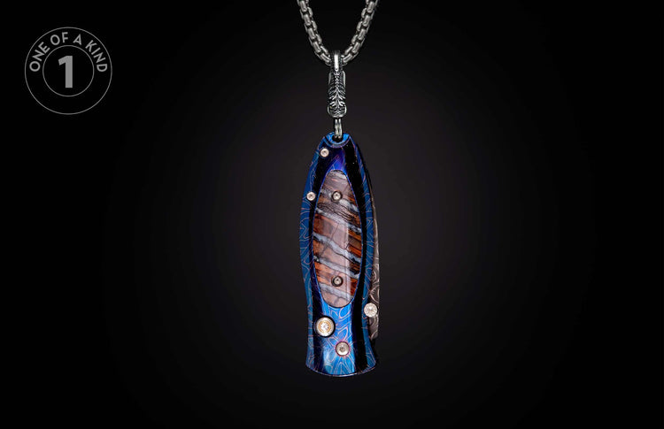 Decorative knife-shaped pendant featuring blue etched metal, a veined stone inlay, and clear gems, on a silver chain.