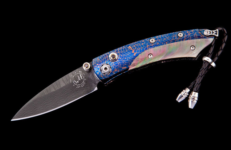 Folding knife with Damascus steel blade, blue and copper patterned handle, iridescent mother-of-pearl inlay, and black braided leather lanyard.