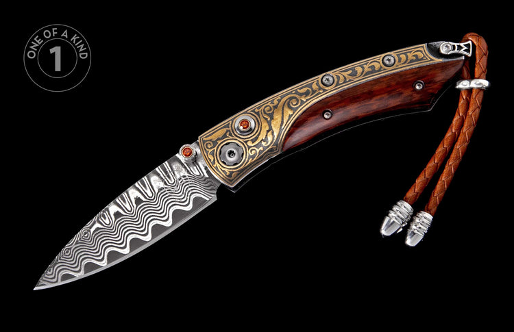 Folding knife with Damascus steel blade, dark wood handle, gold-toned engraved bolsters with orange gemstones, and a braided leather lanyard.