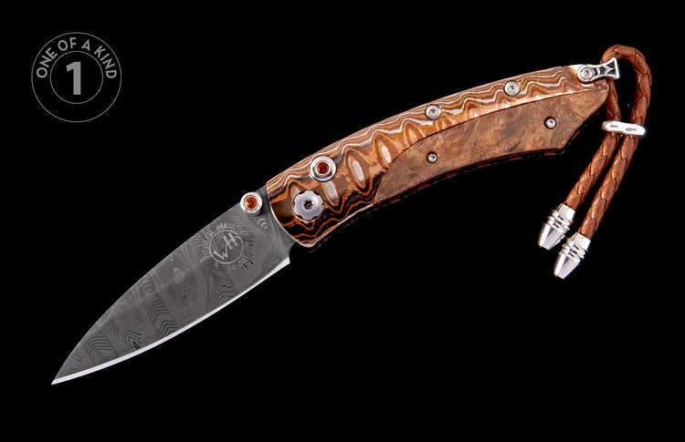 A custom folding knife with a wavy Damascus steel blade and wood handle, featuring red gem accents and a braided leather lanyard.