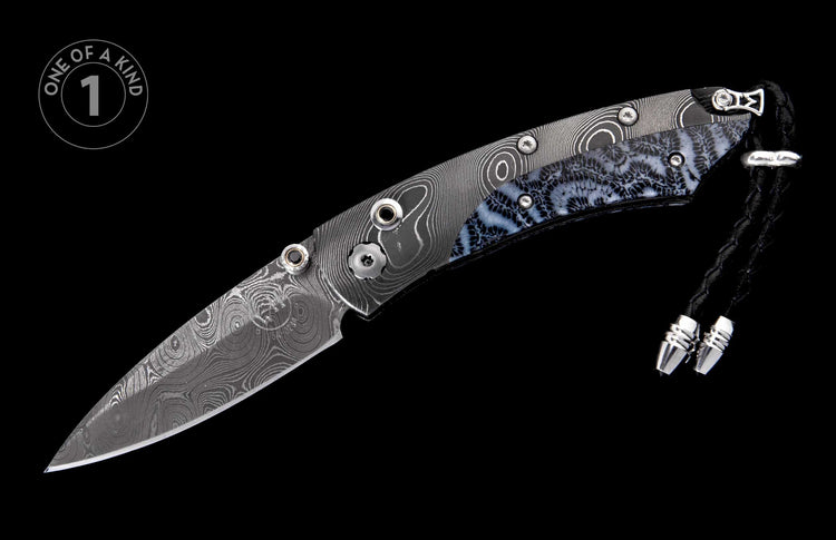 Damascus steel knife with swirling blade and blue-grey patterned fossil coral handle, featuring a black lanyard and a "ONE OF A KIND 1" badge.
