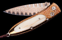 Folding knife with a wavy Damascus steel blade and an ornate bronze handle featuring a light ivory inlay.