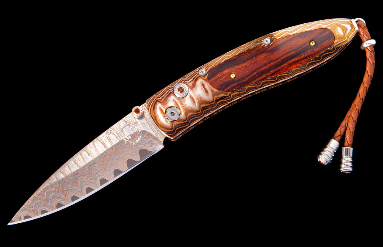 Damascus steel knife with a reddish-brown wooden handle, bronze-toned wavy accents, and a braided brown leather lanyard.