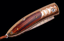 Folding knife with a dark wood handle, layered metal scales featuring copper and silver patterns, and a brown leather strap.