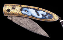 Ornate folding knife with a gold engraved handle featuring a carved blue dragon inlay with gems, and a Damascus steel blade.