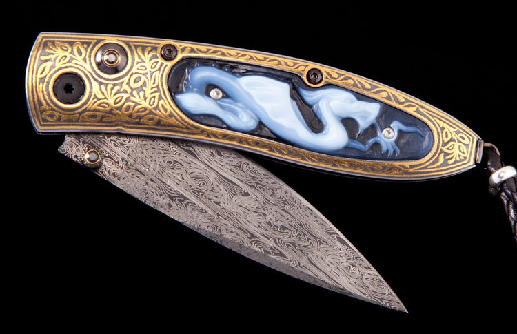 Ornate folding knife with a gold engraved handle featuring a carved blue dragon inlay with gems, and a Damascus steel blade.