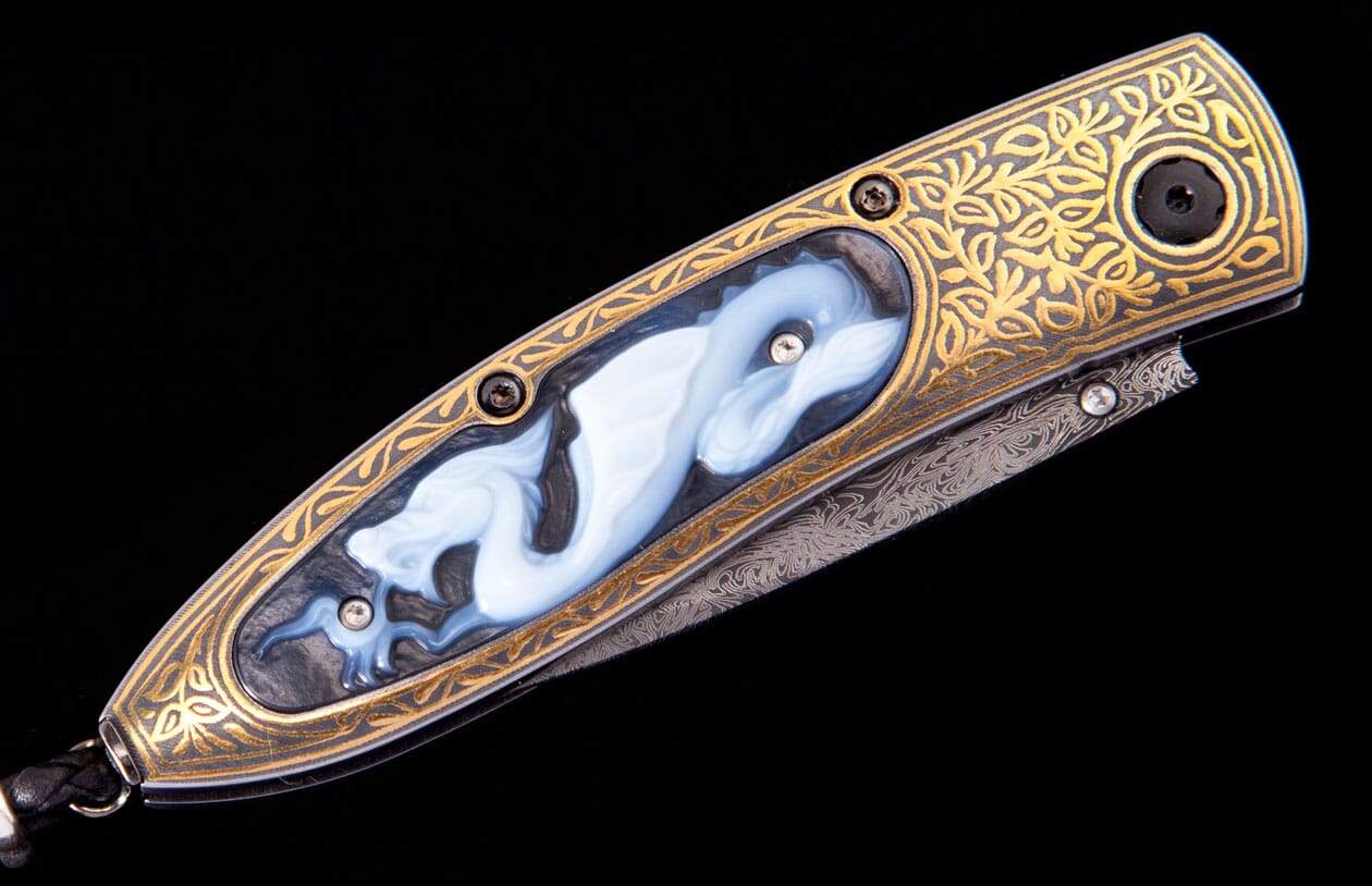 Gold and black ornate knife with a white carved dragon insert, gold leaf engraving, and a patterned Damascus blade.
