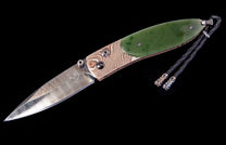 Knife with a wavy Damascus blade and handle with green jade and patterned metal by Gump's Exclusive, detailed with a braided black leather lanyard with silver tips.