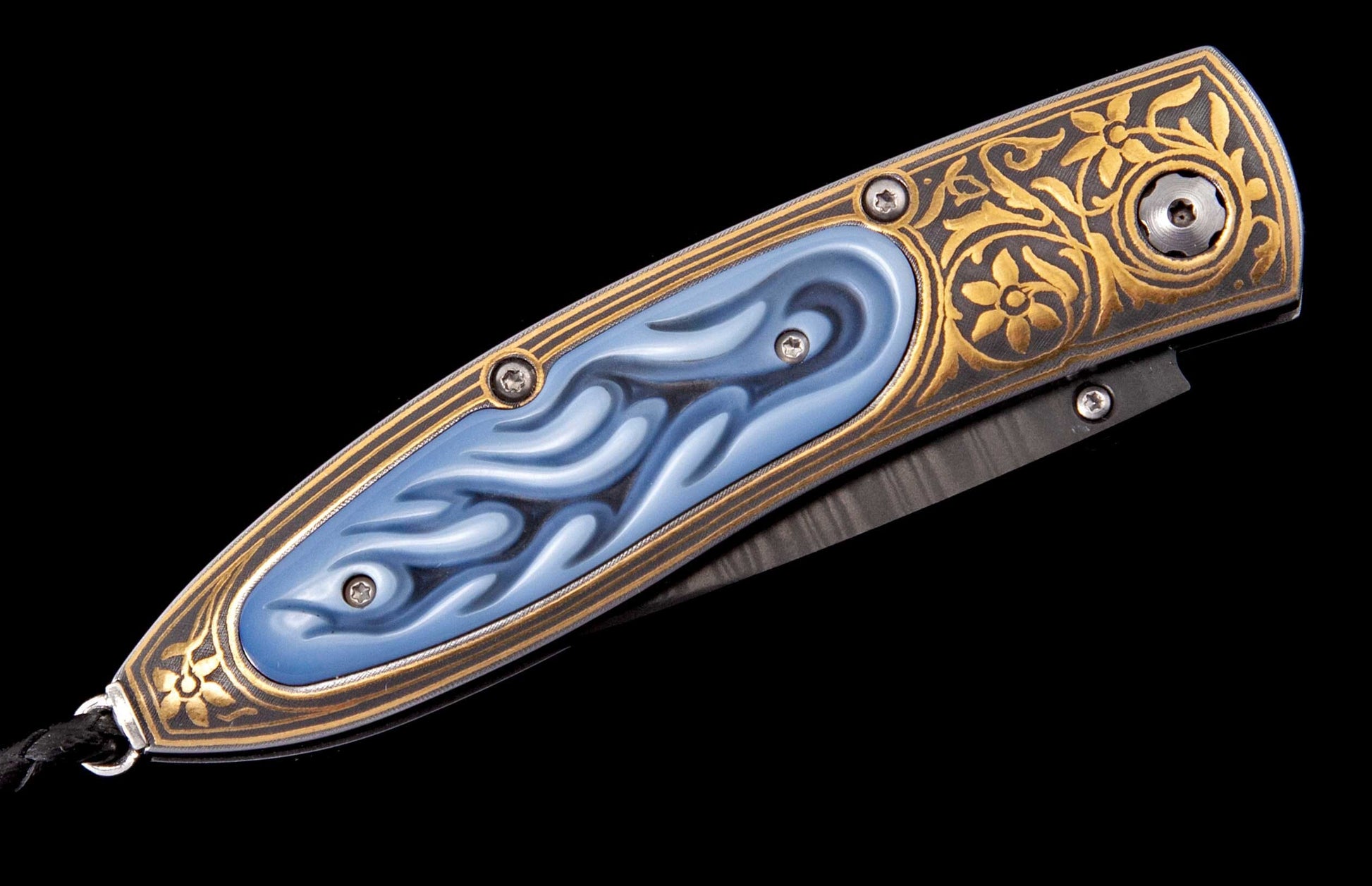 A decorative folding knife with a gold and dark grey engraved handle, featuring a blue wavy inlay and a black lanyard.